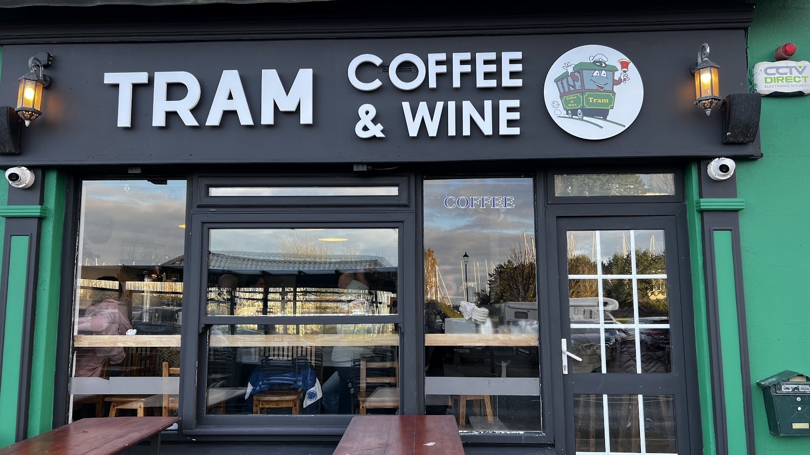 The dark charcoal and teal-green shopfront of Tram Coffee & Wine on Harbour Road, Howth, with the tram mascot logo and outdoor tables
